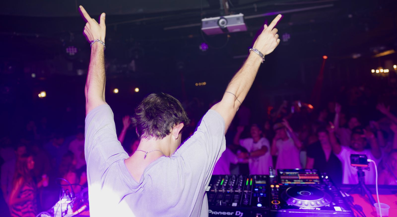 Ricky Lime playing to a packed room, arms up behind the decks